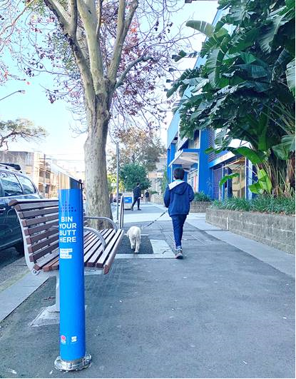 Person walking dog past cigarette butt litter bin