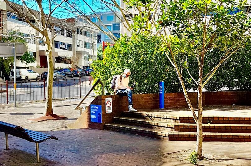 Man sitting outdoors near butt litter signage and bin